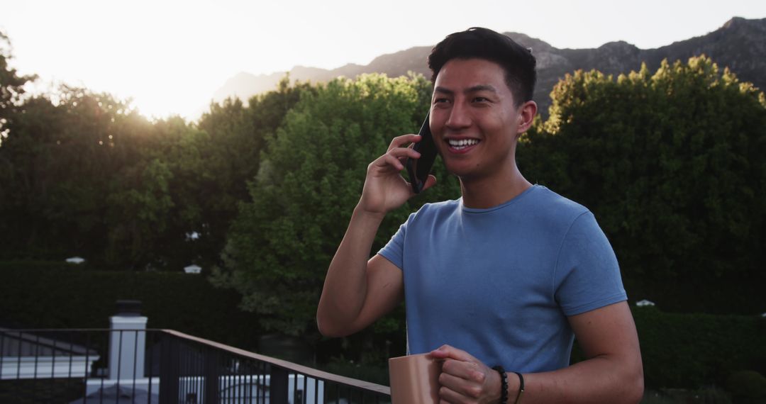 Smiling Man Relaxing with Coffee and Phone at Sunset on Balcony