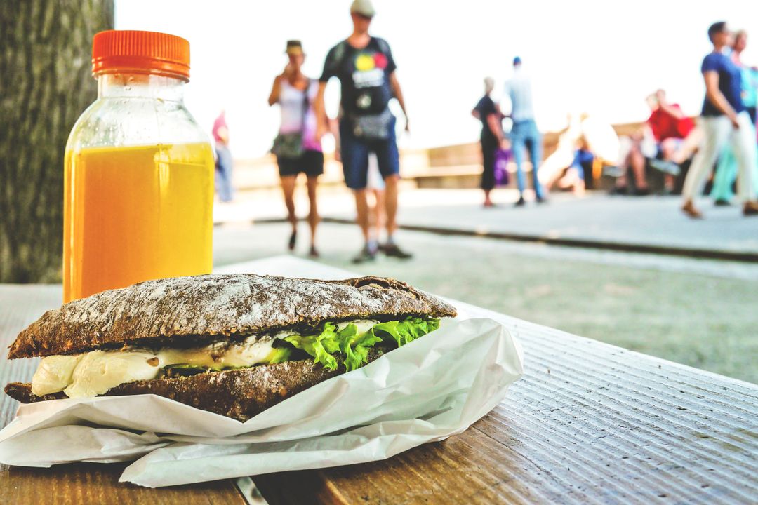 Rustic rye sandwich with creamy cheese and fresh lettuce and orange juice on bench