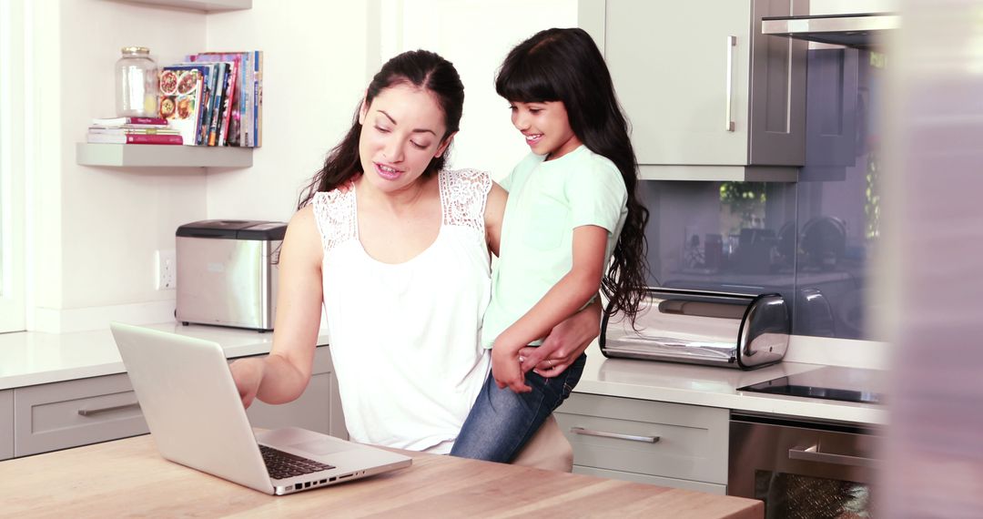 Mother Holding Daughter While Using Laptop in Modern Kitchen - Free Images, Stock Photos and Pictures on Pikwizard.com