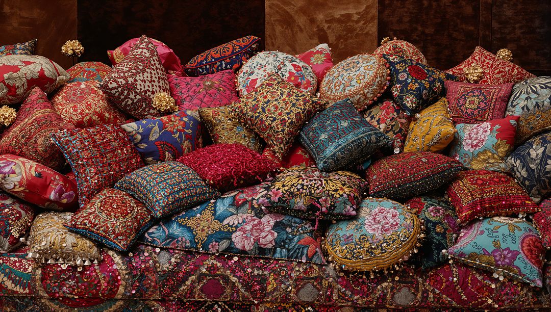 Piled embroidered cushions on patterned velvet sofa showcasing ornate tassels and beads