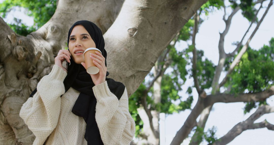 Young Muslim Woman Holding Coffee Cup and Talking on Phone Outdoors - Free Images, Stock Photos and Pictures on Pikwizard.com