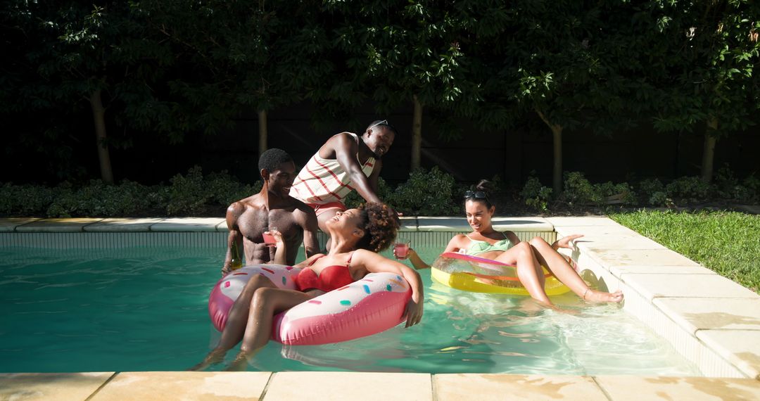 Friends Relaxing in Pool on Ring Floats with Drinks