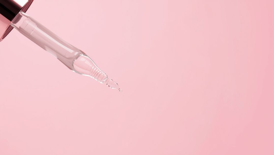 Elegant Glass Pipette Droplet on Pink Background for Skincare Concepts