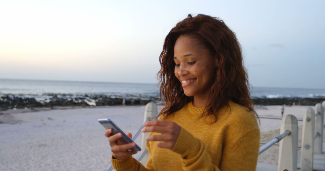 Young Woman Smiling and Using Smartphone at the Beach - Free Images, Stock Photos and Pictures on Pikwizard.com