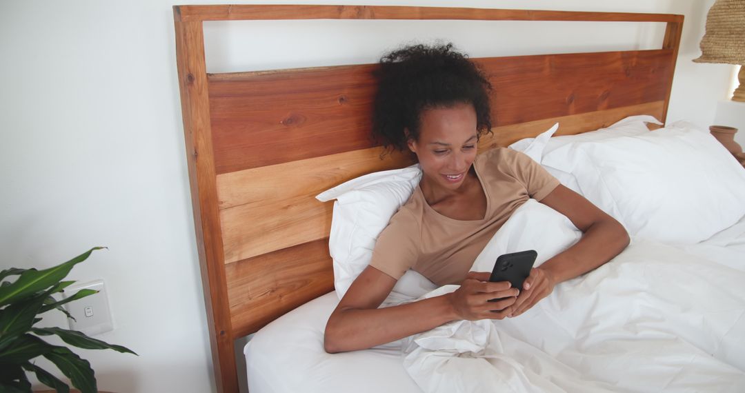 Woman Relaxing in Bed with Smartphone Surrounded by Minimalist Decor