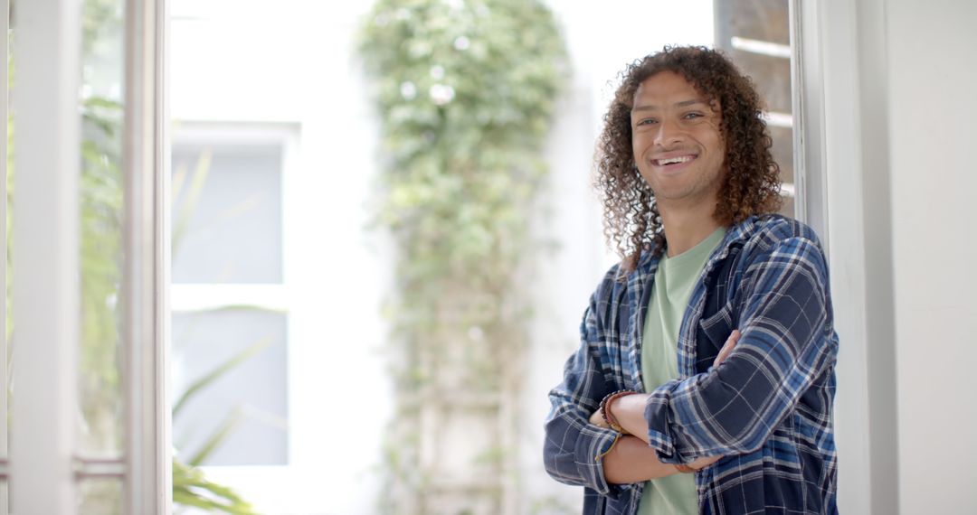 Casual Young Man with Curly Hair Smiling and Crossing Arms Indoors - Free Images, Stock Photos and Pictures on Pikwizard.com