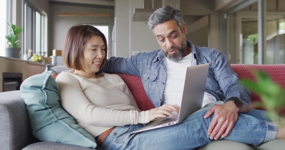 Smiling interracial couple using laptop on cozy sofa at home - Free Images, Stock Photos and Pictures on Pikwizard.com