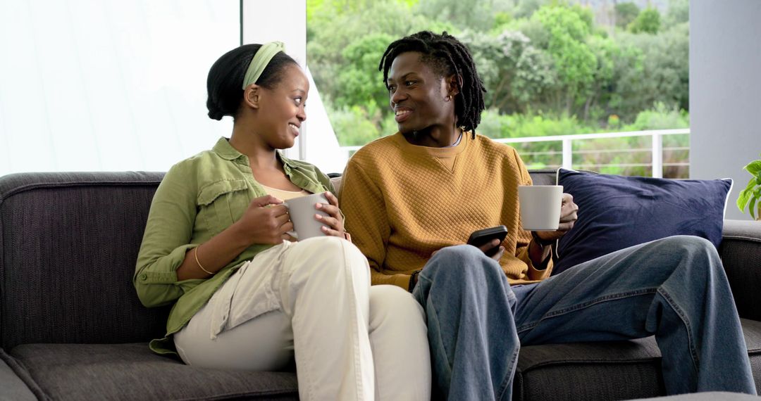 African American couple sharing coffee and conversation on sofa by balcony with greenery
