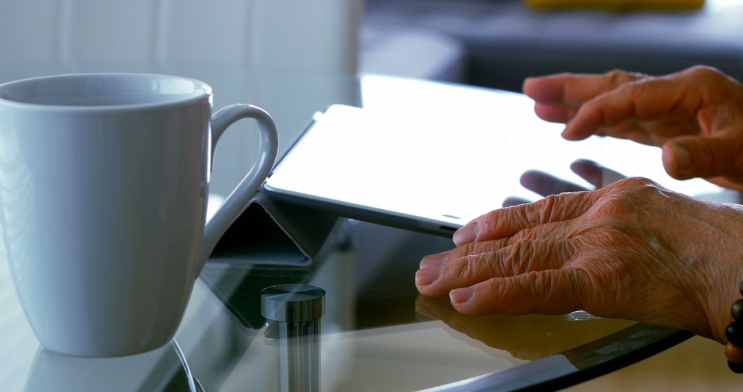 Elderly Hands Using Digital Tablet with Coffee Mug on Glass Table - Free Images, Stock Photos and Pictures on Pikwizard.com