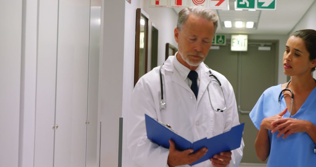 Experienced Doctor Discussing Patient Chart with Nurse in Hospital Corridor - Free Images, Stock Photos and Pictures on Pikwizard.com