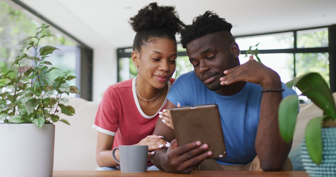 Image of happy african american couple sitting on sofa and using tablet - Free Images, Stock Photos and Pictures on Pikwizard.com
