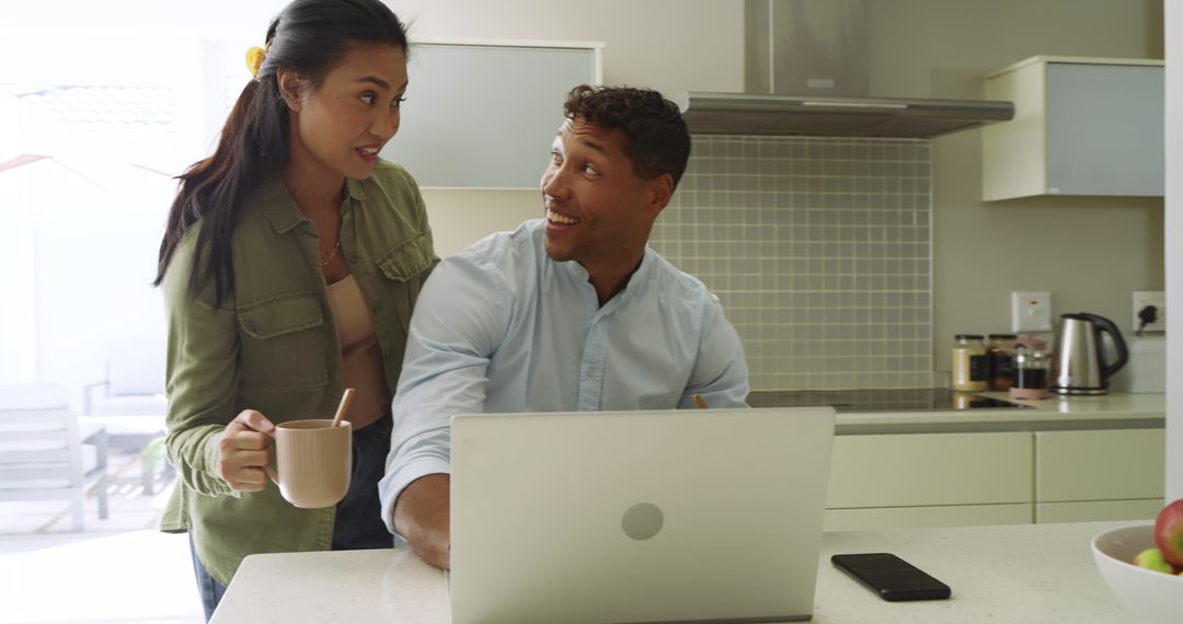 Remote couple working together at sunlit kitchen island with laptop and coffee
