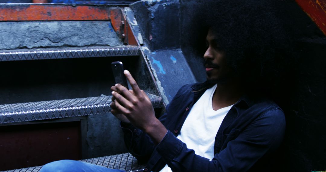 Young Man with Afro Hair Using Smartphone on Urban Stairs - Free Images, Stock Photos and Pictures on Pikwizard.com