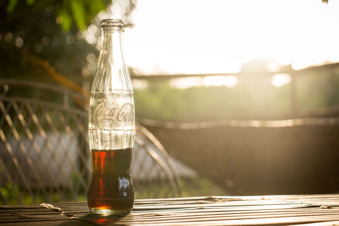 Refreshing Cola Bottle on Wooden Table During Sunset Outdoors - Free Images, Stock Photos and Pictures on Pikwizard.com