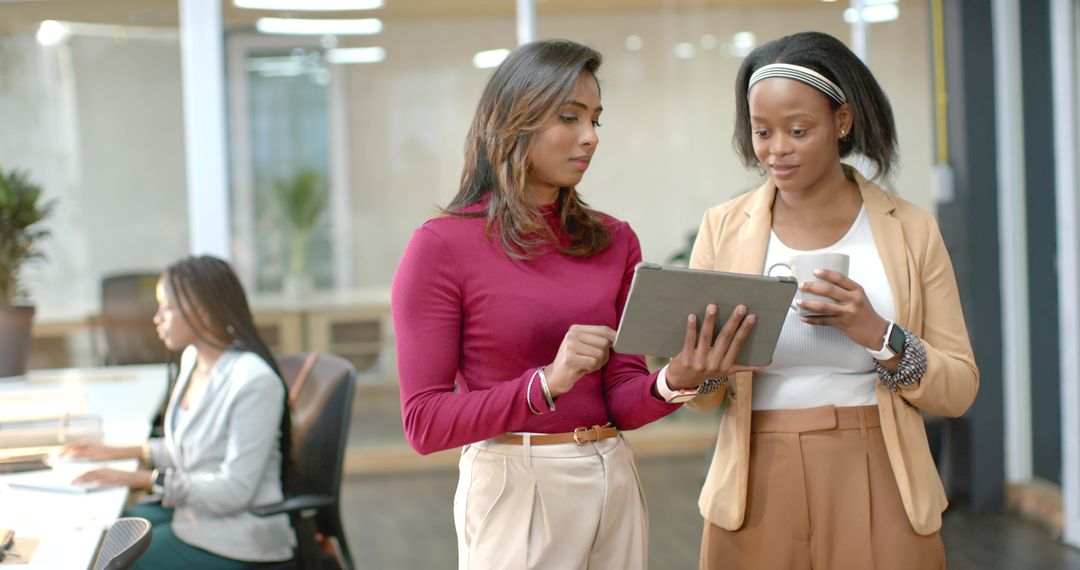 Female colleagues reviewing tablet and collaborating in modern open-plan office