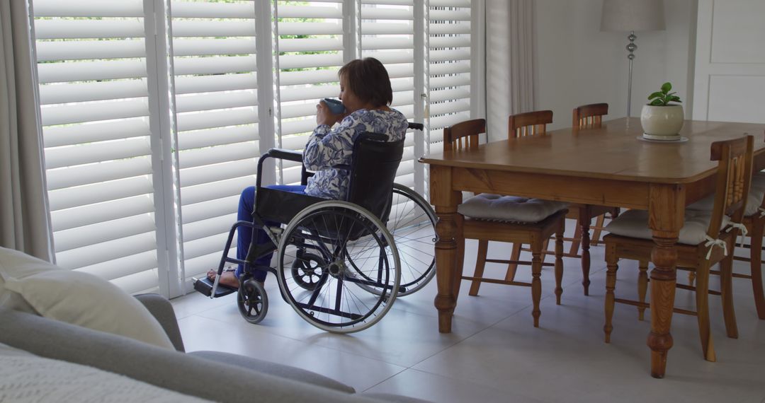 Woman in wheelchair looking through blinds in modern home - Free Images, Stock Photos and Pictures on Pikwizard.com