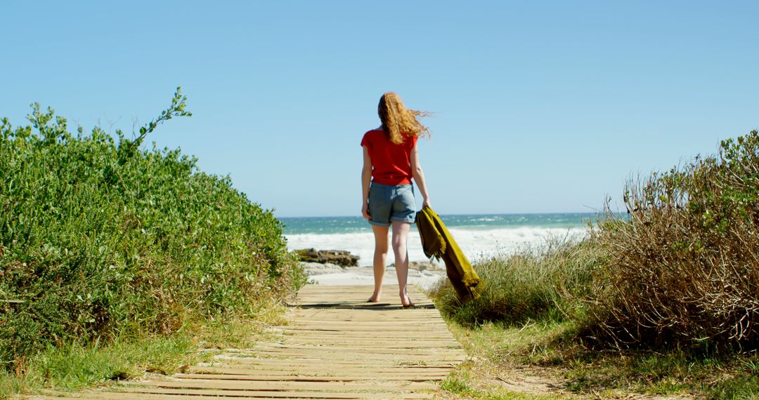 Woman Walking Toward Ocean on Wooden Pathway on Sunny Day - Free Images, Stock Photos and Pictures on Pikwizard.com