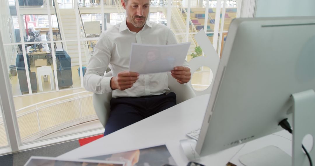 Businessman Analyzing Documents in Modern Office with Computer - Free Images, Stock Photos and Pictures on Pikwizard.com