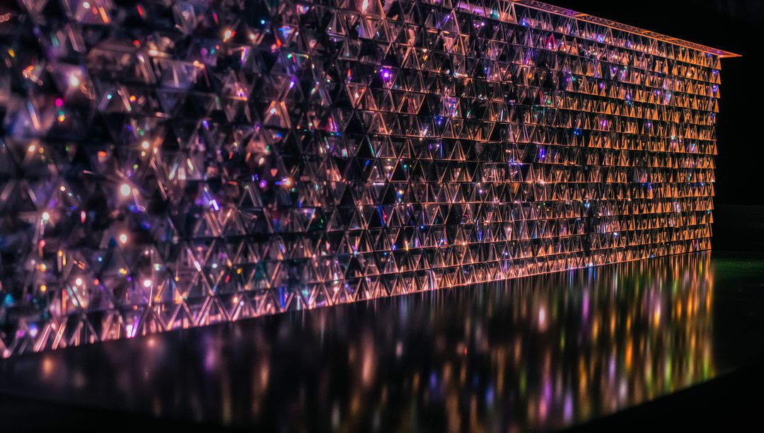 Glowing prism wall with multicolor LED refractions and black floor reflections, triangular modules