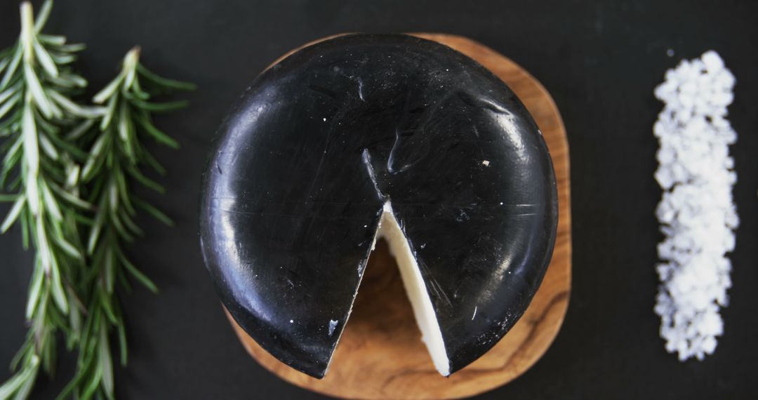 A wheel of black cheese with a piece cut out is presented on a wooden board, with copy space - Free Images, Stock Photos and Pictures on Pikwizard.com