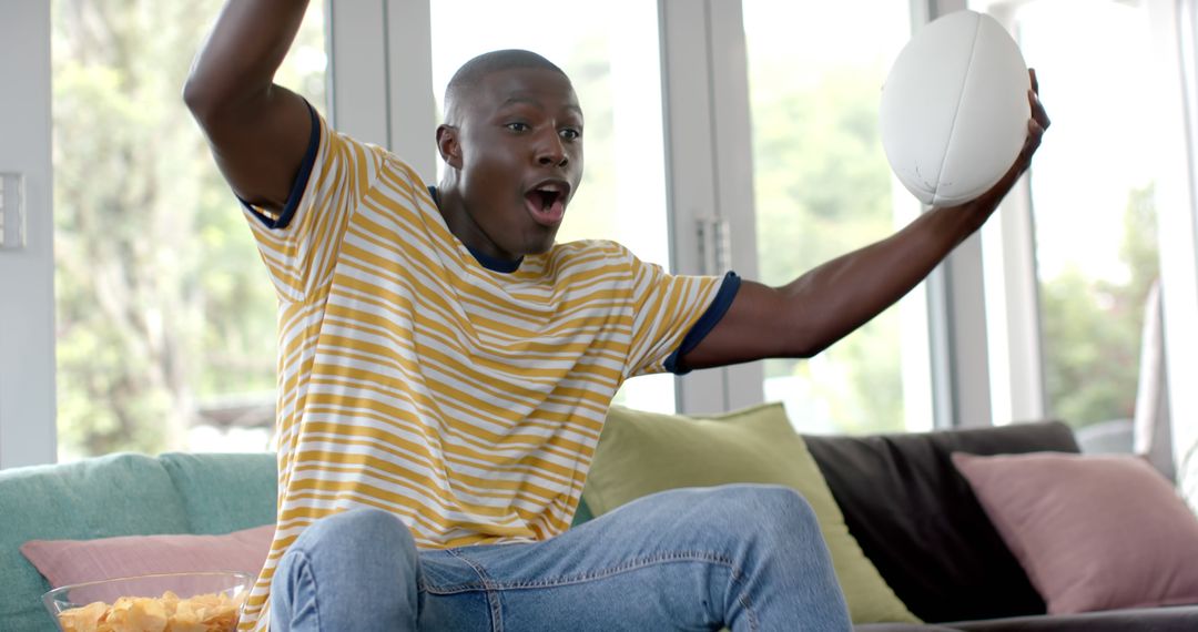 Excited Man Cheering on Sports Team while Holding Football - Free Images, Stock Photos and Pictures on Pikwizard.com