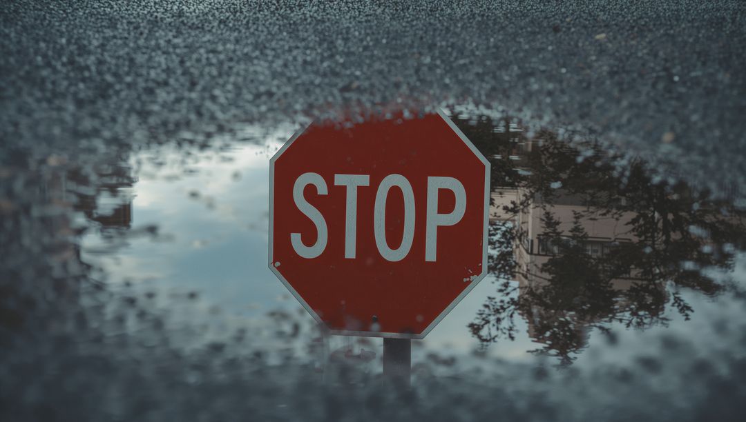 Rain-Puddled Stop Sign Reflection on Wet Asphalt Road, Moody Urban Traffic Concept