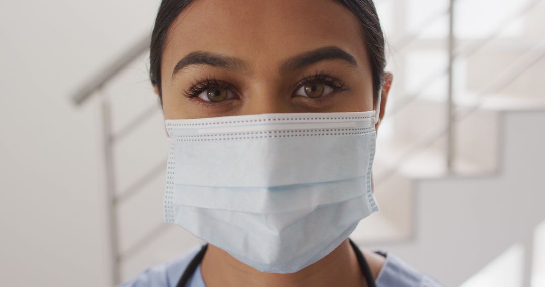 Image of biracial female doctor putting on face mask looking at camera - Free Images, Stock Photos and Pictures on Pikwizard.com