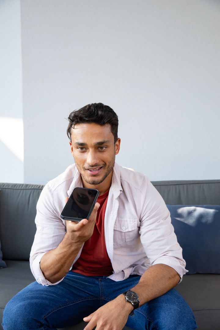 Casually Relaxed Man Speaking into Smartphone at Home on Sofa