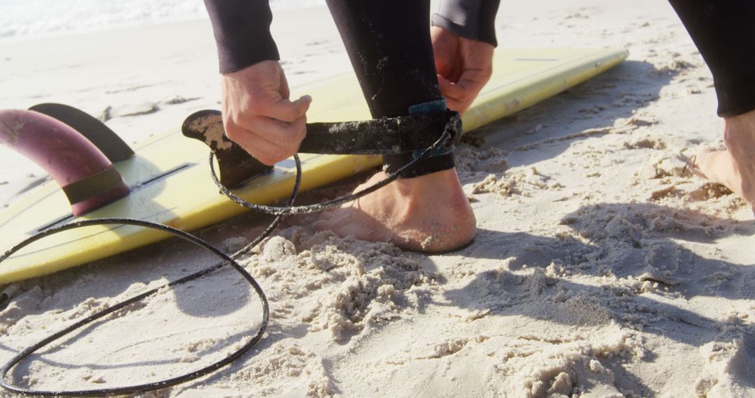 Surfer fastening ankle leash next to surfboard on sandy beach - Free Images, Stock Photos and Pictures on Pikwizard.com