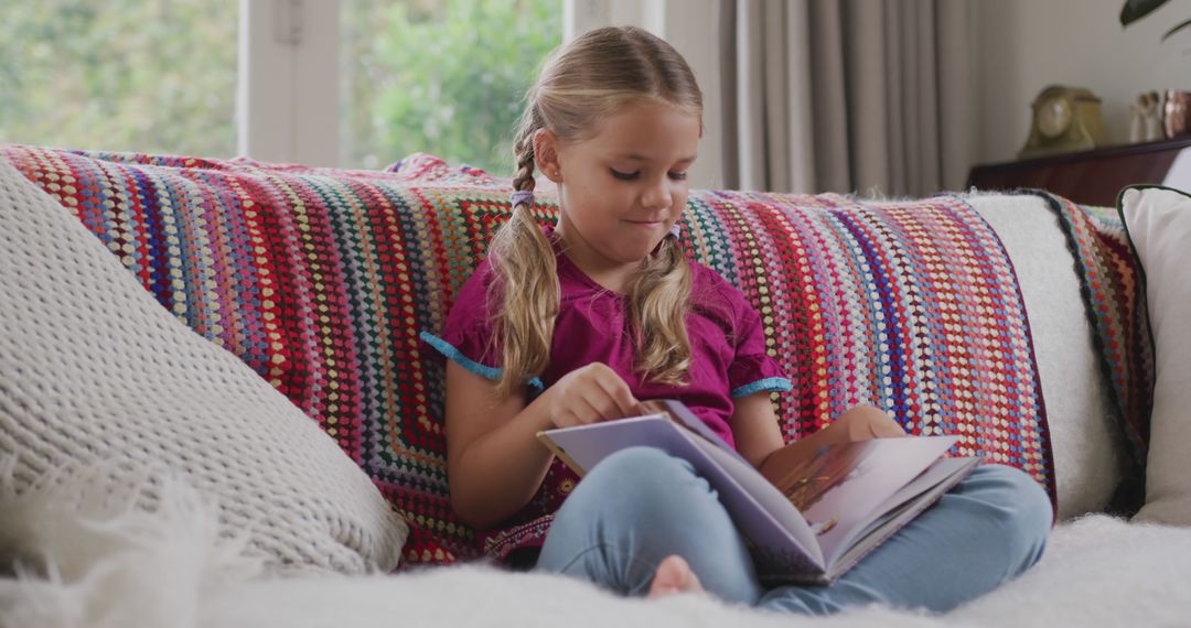 Young Girl Reading Book on Colorful Couch at Home - Free Images, Stock Photos and Pictures on Pikwizard.com