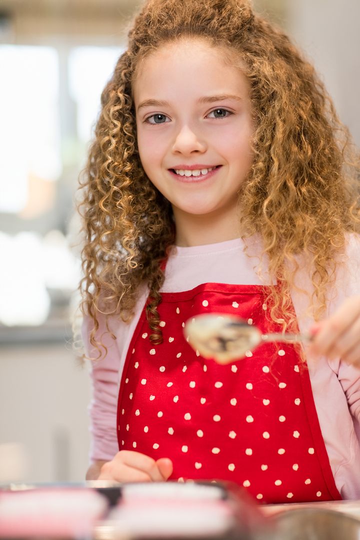 Smiling Girl Baking Muffins with Red Polka Dot Apron in Kitchen