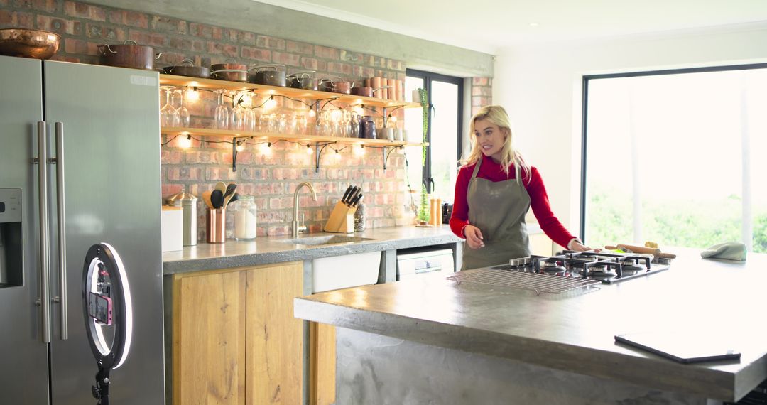 Sunlit rustic modern kitchen cooking scene with woman in grey apron at concrete island