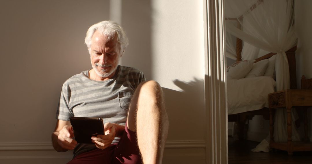 Senior Man Relaxing at Home Reading Tablet in Sunny Room - Free Images, Stock Photos and Pictures on Pikwizard.com