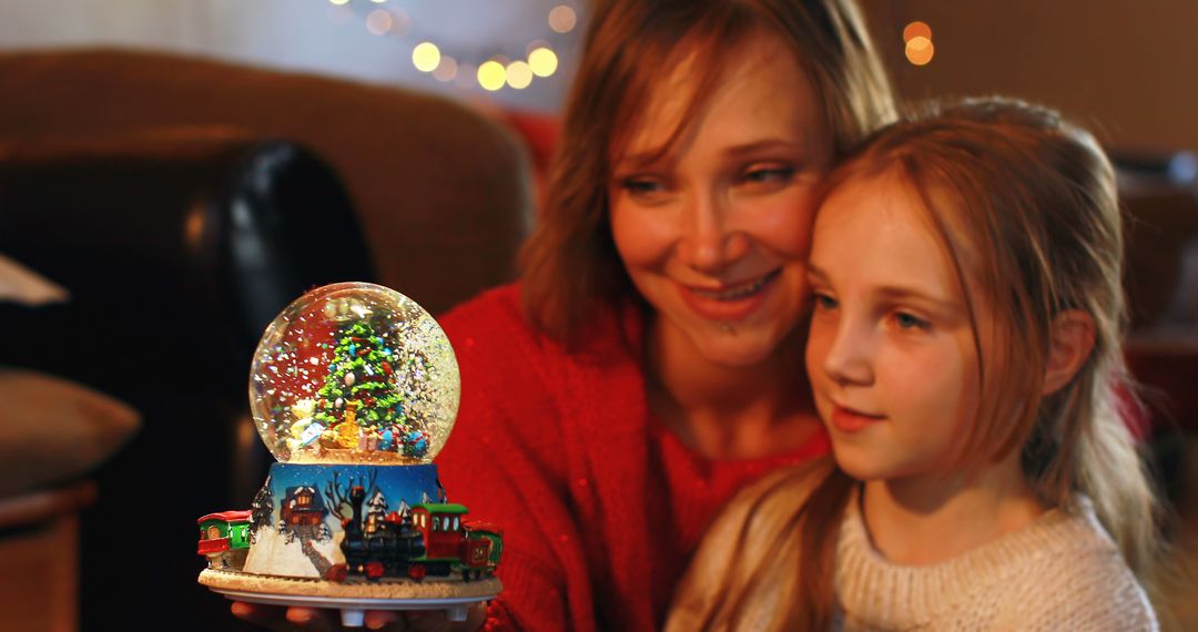 Mother and daughter enjoying Christmas snow globe indoors - Free Images, Stock Photos and Pictures on Pikwizard.com