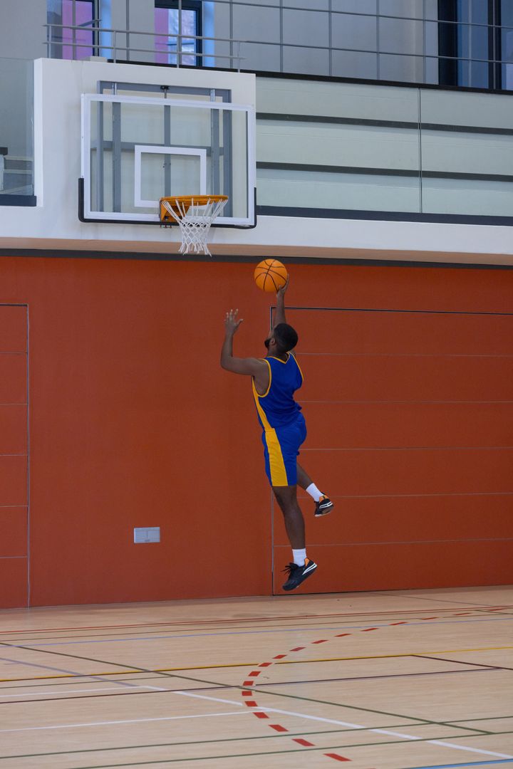Athletic Male Basketball Player Performing Layup in Gym