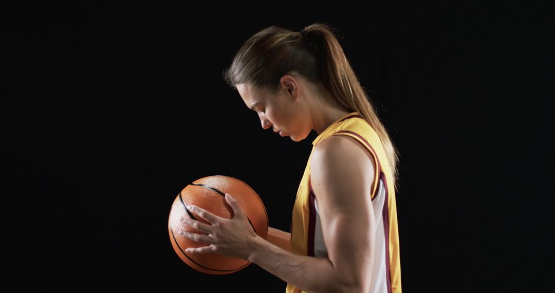 Determined Female Basketball Player Gripping Ball in Dark Atmosphere