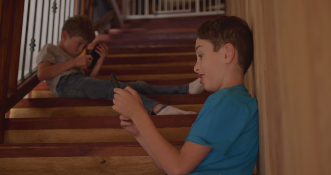 Two Boys Playing Games on Smartphones Sitting on Wooden Stairs - Free Images, Stock Photos and Pictures on Pikwizard.com