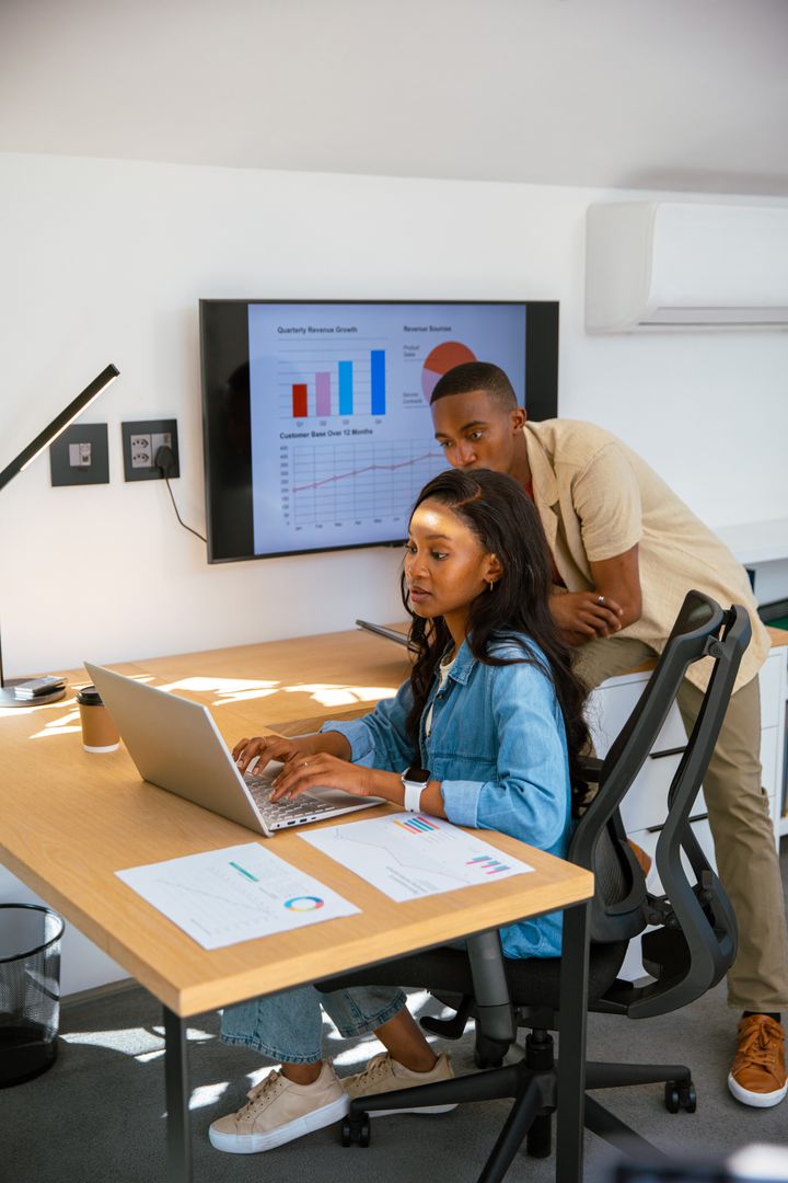 Coworkers Analyzing Quarterly Data on Laptop and Monitor in Office