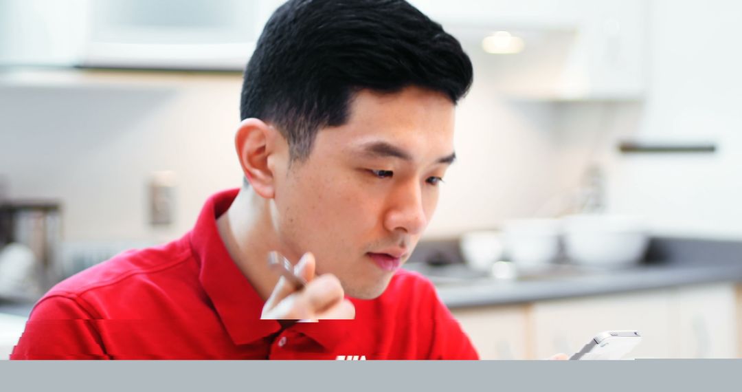 Asian Man Engaged with Smartphone While Eating Breakfast at Home
