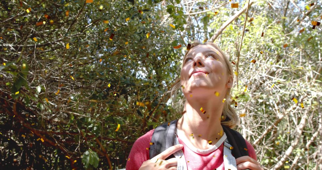 Contemplative hiker looking up through sunlit woodland canopy while gripping backpack