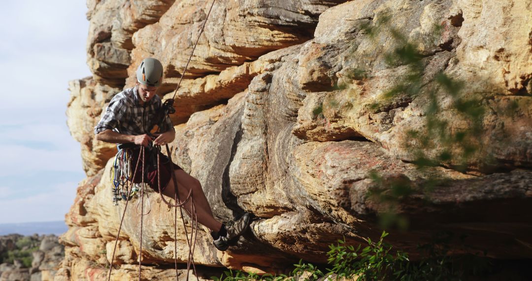 Rock climber scaling cliff while securing gear in arid landscape - Free Images, Stock Photos and Pictures on Pikwizard.com