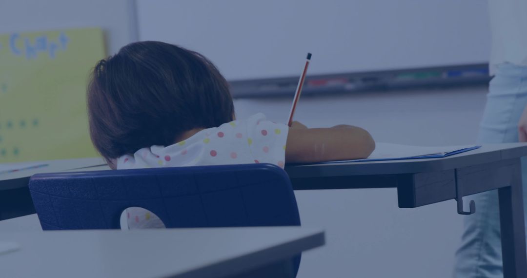 Young Student Writing on Desk in Classroom