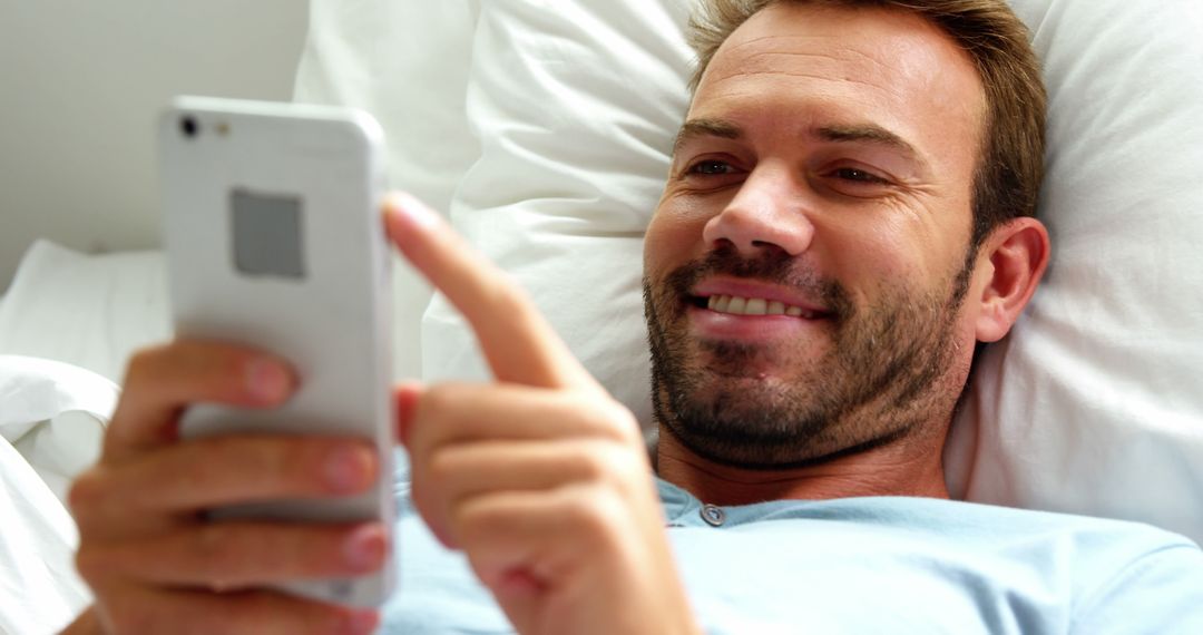 Man Smiling While Using Smartphone Relaxing in Bed - Free Images, Stock Photos and Pictures on Pikwizard.com