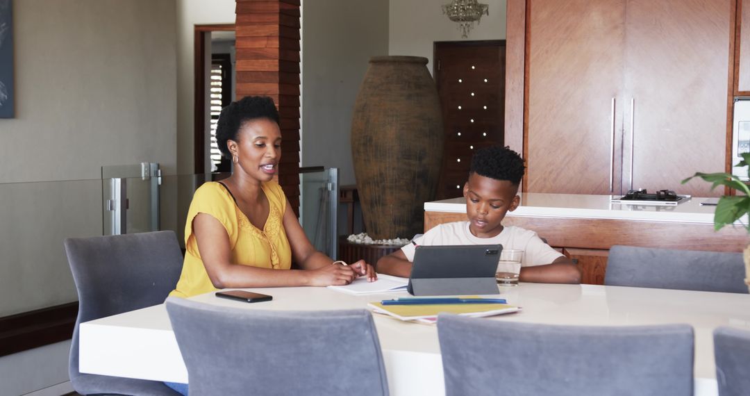African American mother tutoring son with tablet at dining table in modern kitchen