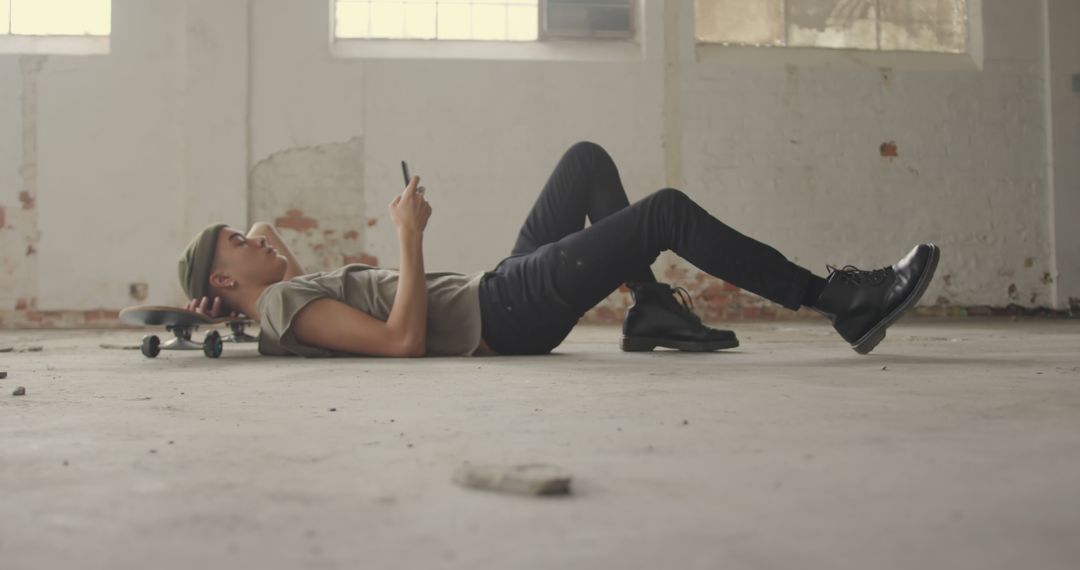 Young Man Lying on Skateboard Using Smartphone in Industrial Space - Free Images, Stock Photos and Pictures on Pikwizard.com