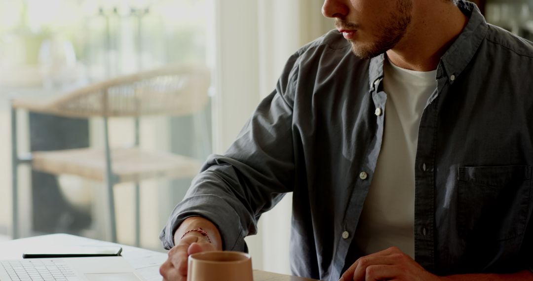 Man Holding Mug, Focused on Writing Notes by Sunny Window