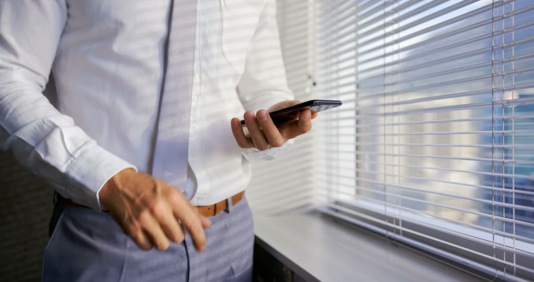 Businessman Checking Smartphone in Office Near Window Blinds