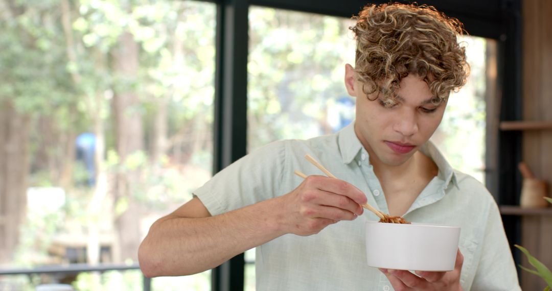 Young Man Enjoying Noodles with Chopsticks in Bright Kitchen