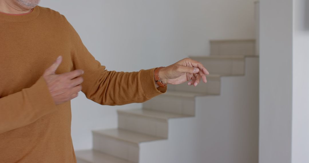 Person in Brown Sweater Gesturing Near Modern Staircase