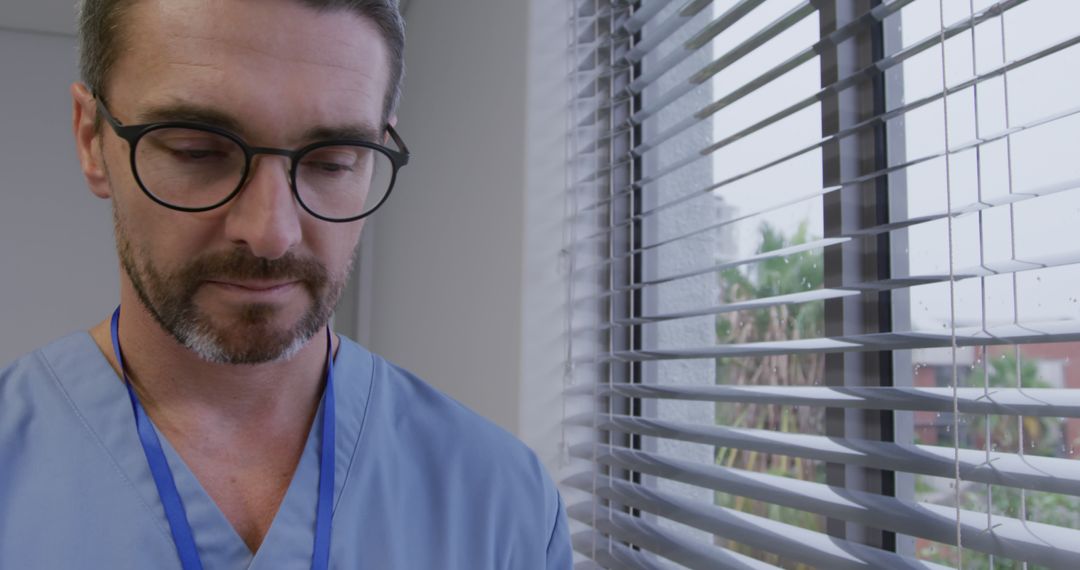 Tired Male Doctor in Scrubs Standing Near Window with Blinds - Free Images, Stock Photos and Pictures on Pikwizard.com